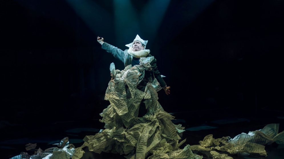 Phelim McDermott wrapped in lots of scrunched up sheet music, wearing a paper hat
