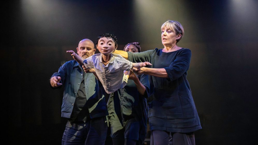 Three puppeteers move to make a small puppet of a boy fly through the air