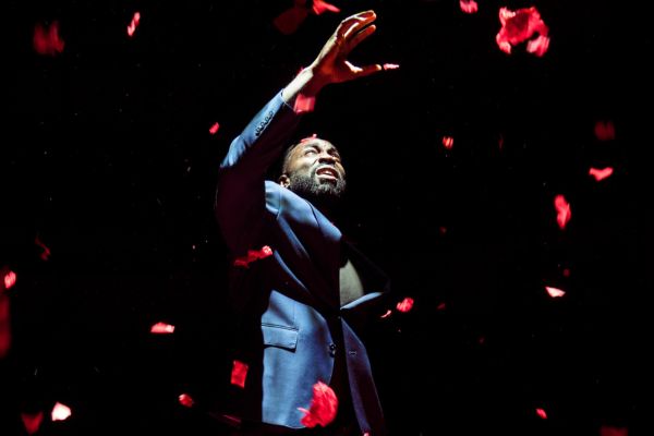 Delroy (played by Paapa Essiedu) wears a blue suit, surrounded by falling red confetti