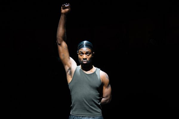 Delroy (played by Paapa Essiedu) holds his fist up in the air