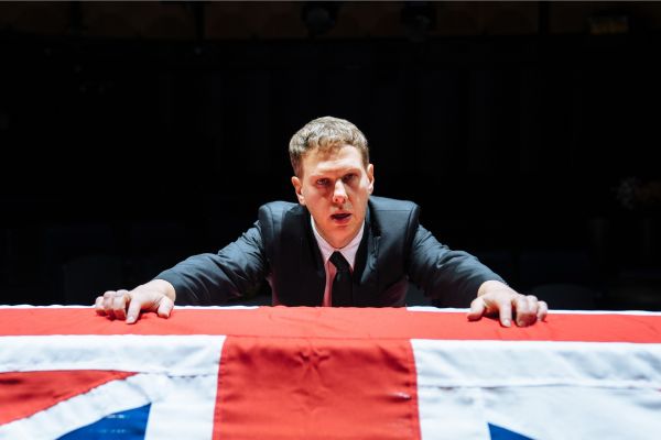 Michael (played by Thomas Coombes) leans on a coffin covered in the Union Jack flag