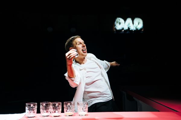 Michael (played by Thomas Coombes) holds a pint glass with empty pint glasses in front of him, with 'DAD' written in the background